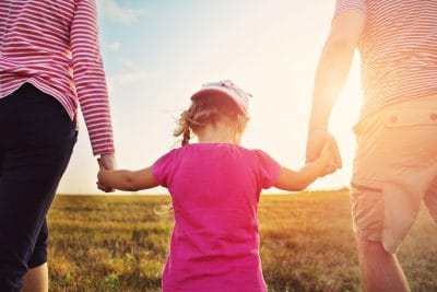 Parents holding daughter’s hands while walking in the countryside and thinking about protecting their family’s financial future